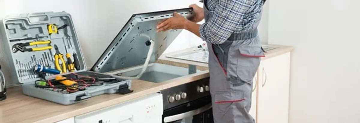 Cooktop repair technician lifting a built-in stovetop for service in Los Angeles, CA