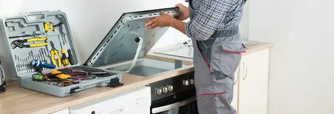 Cooktop repair technician lifting a built-in stovetop for service in Los Angeles, CA