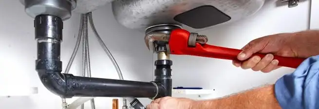 Garbage disposal repair technician tightening the sink drain and disposal connection in Los Angeles, CA