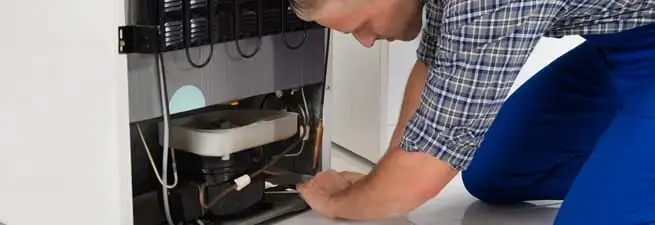 Refrigerator repair technician servicing the compressor and condenser area in Los Angeles, CA