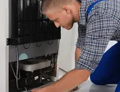 Refrigerator repair technician servicing the compressor and condenser area in Los Angeles, CA