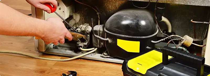 Refrigerator repair technician fixing the compressor and wiring in Los Angeles, CA